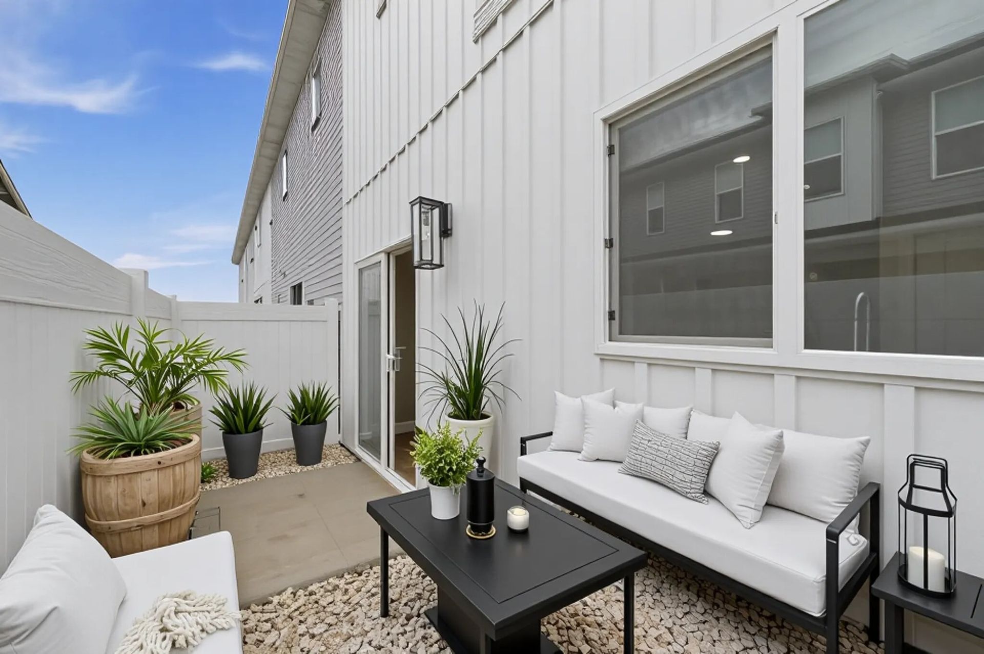 Apartment balcony with white seating, a black coffee table, and potted plants.