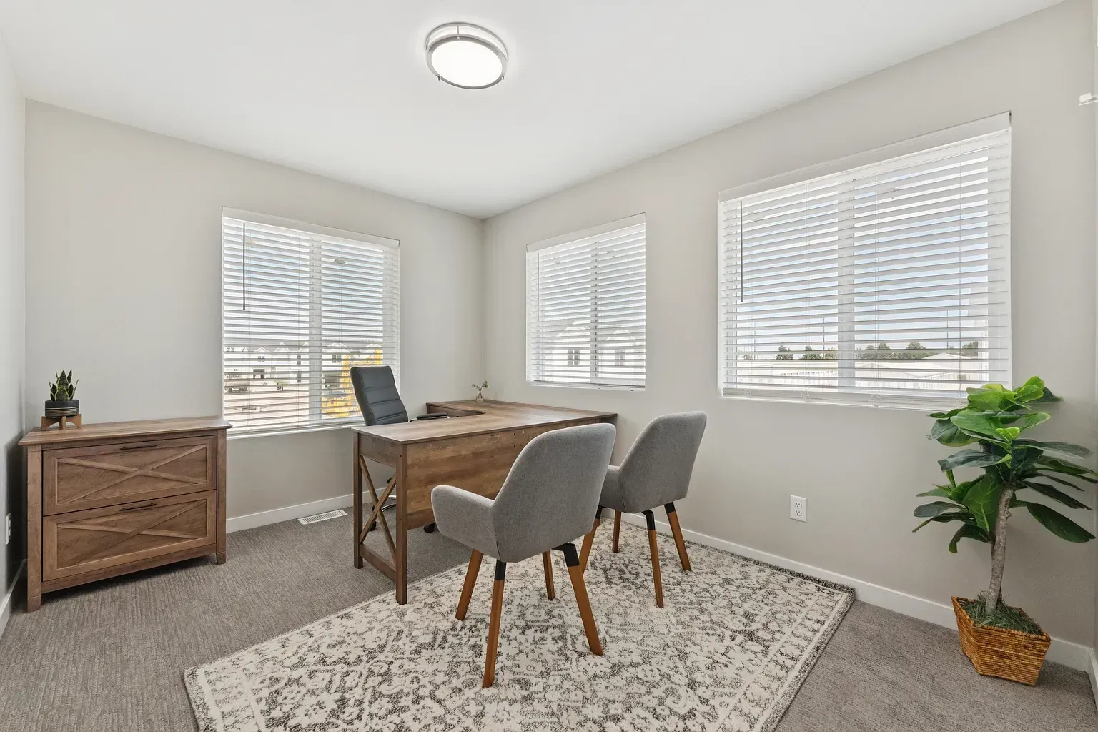 Apartment interior office/study with a wooden desk, three chairs, window blinds, and a potted plant.