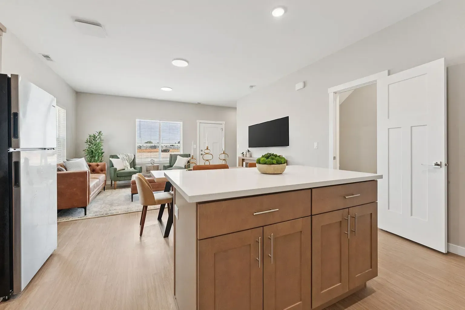 Open-concept kitchen with island, fridge on the left, and a living area with sofa, chairs, and a TV.
