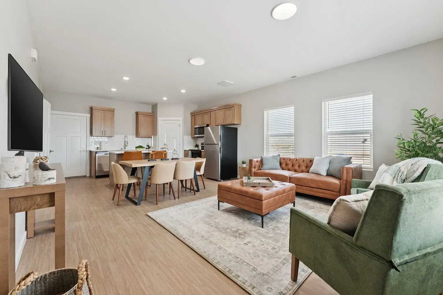 Open-concept living area with dining table, brown leather sofa, and stainless-steel kitchen.