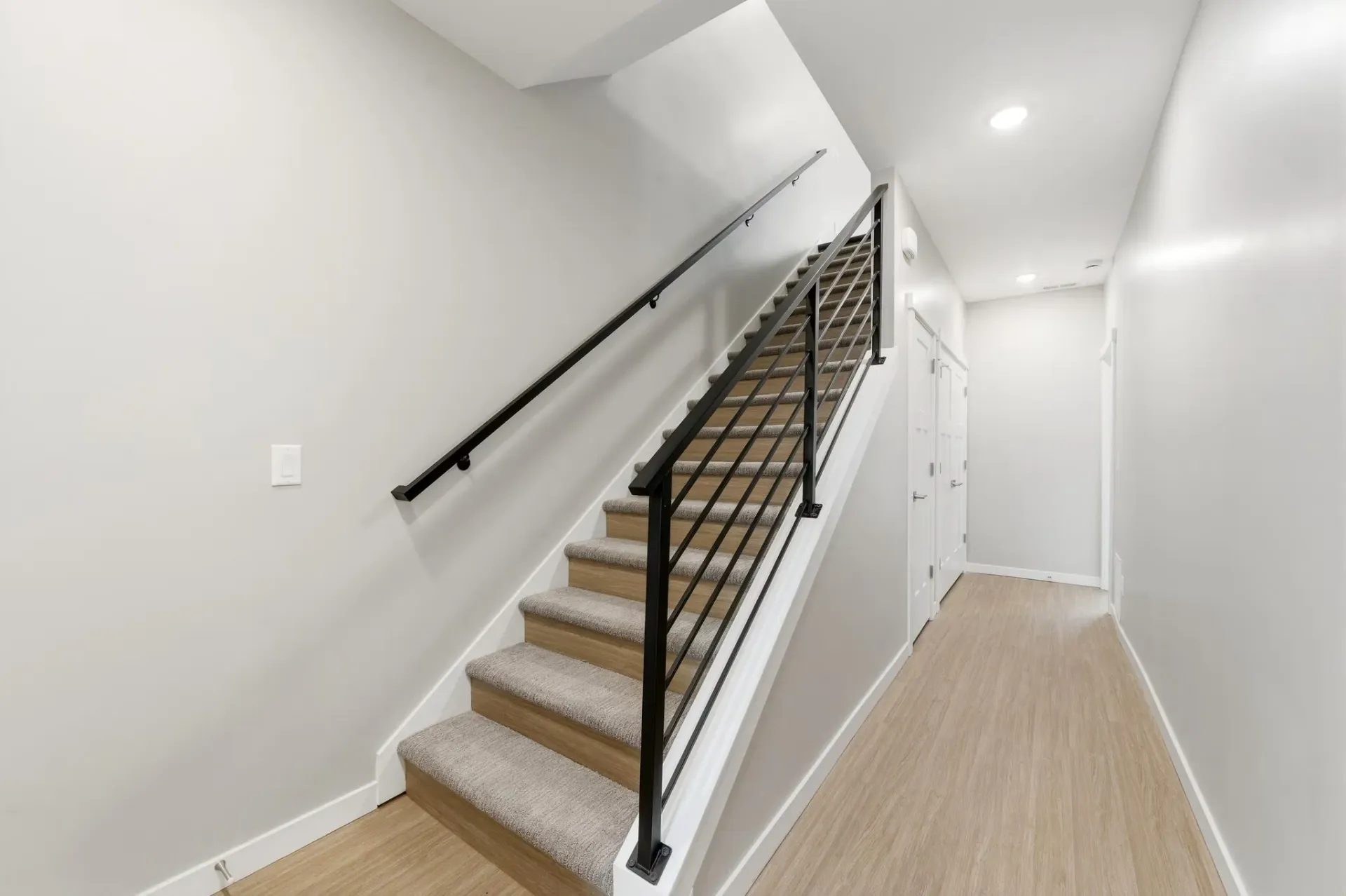 Bright hallway with beige carpet and a black metal stair railing in a modern apartment building.