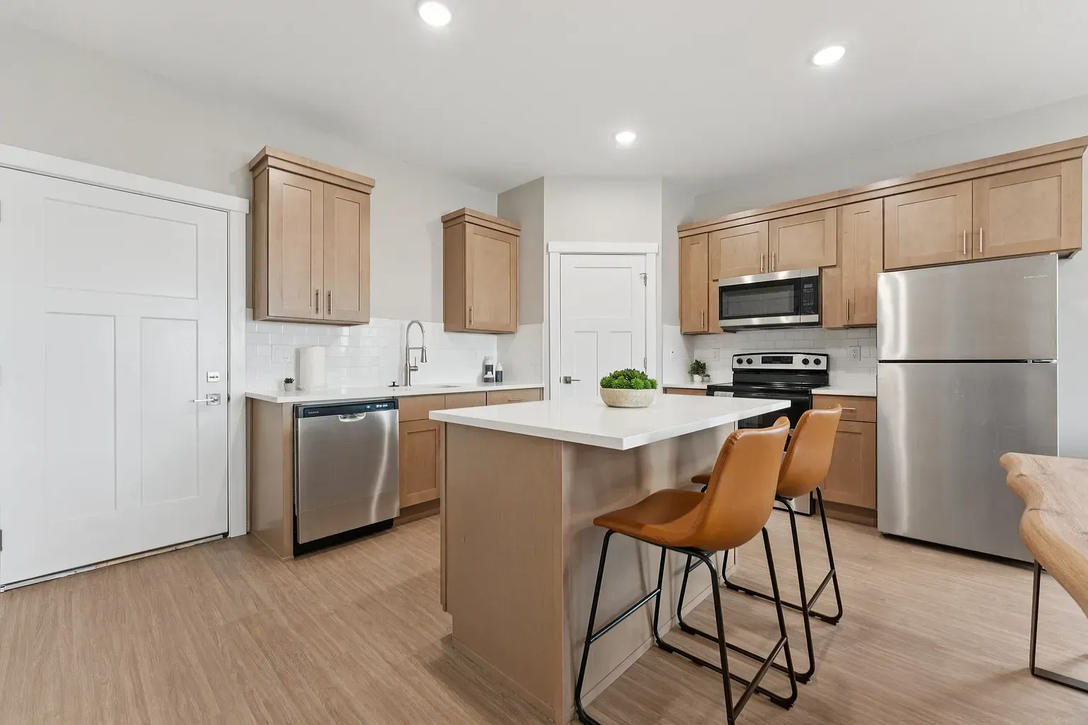 Modern apartment kitchen with an island, light wood cabinets, and stainless-steel appliances.