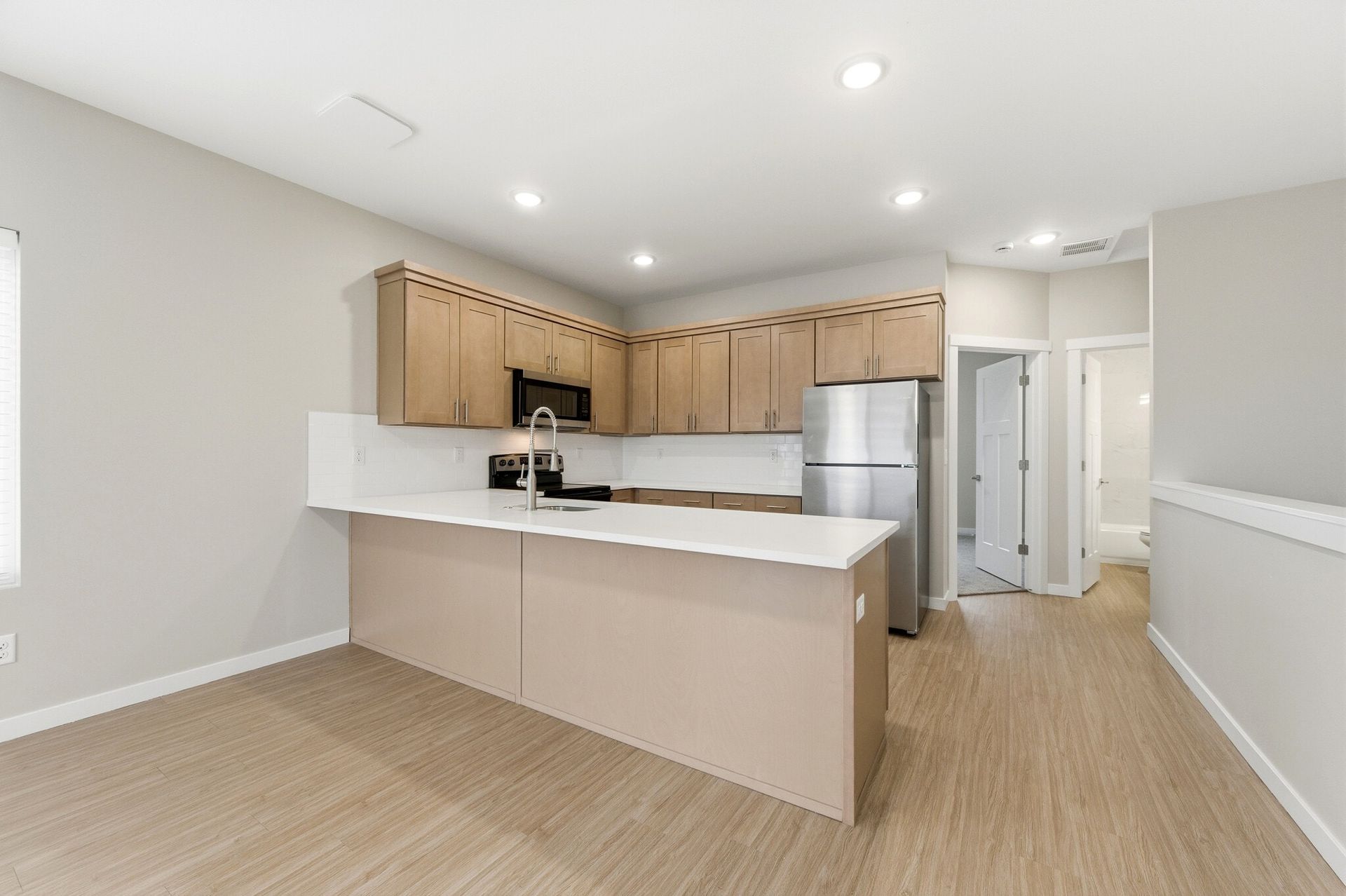 Modern apartment kitchen with light wood cabinets, white countertops, stainless steel appliances, and an island.