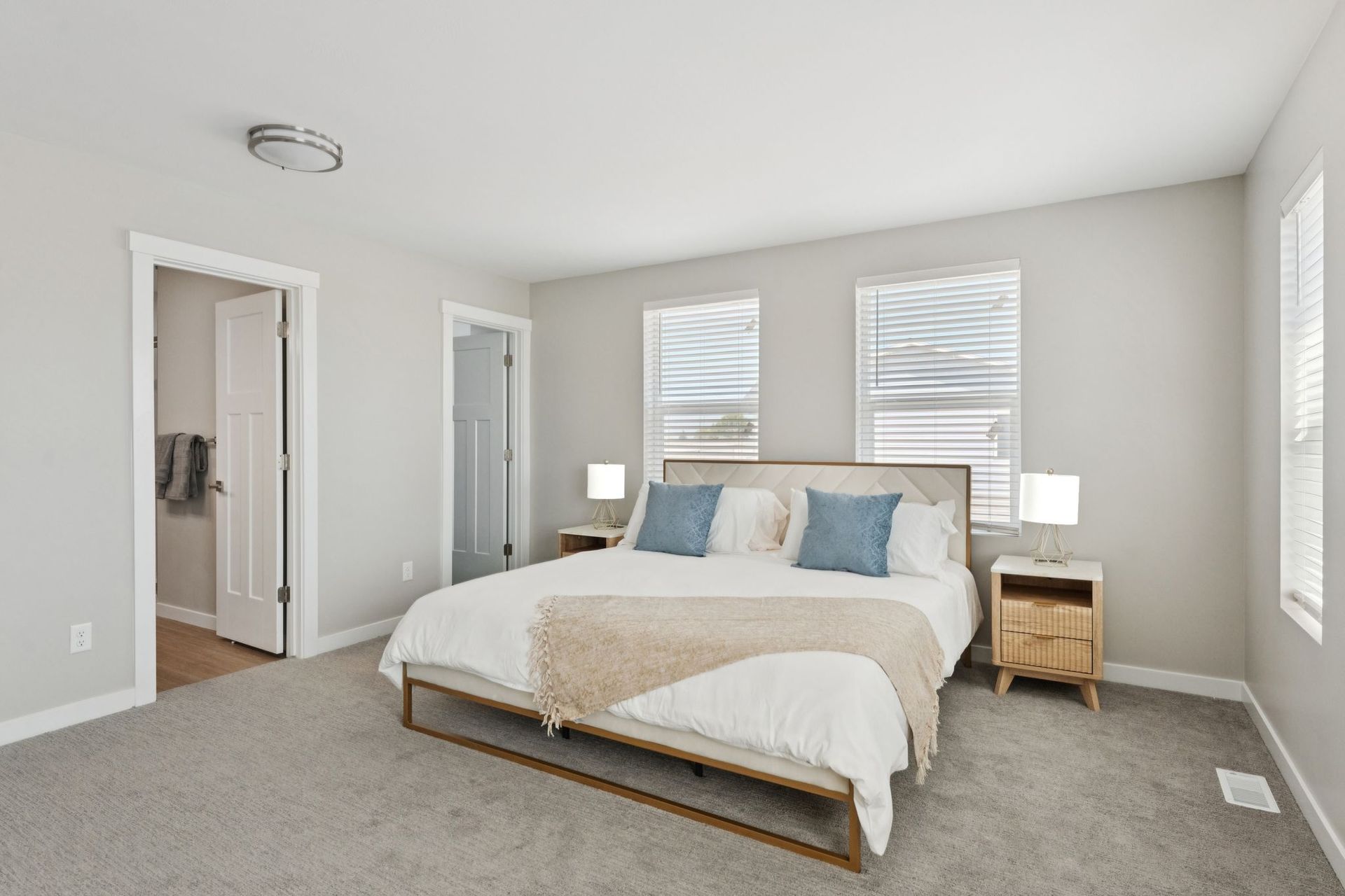 Bedroom with a queen bed, two nightstands, and three windows in a neutral-toned apartment.