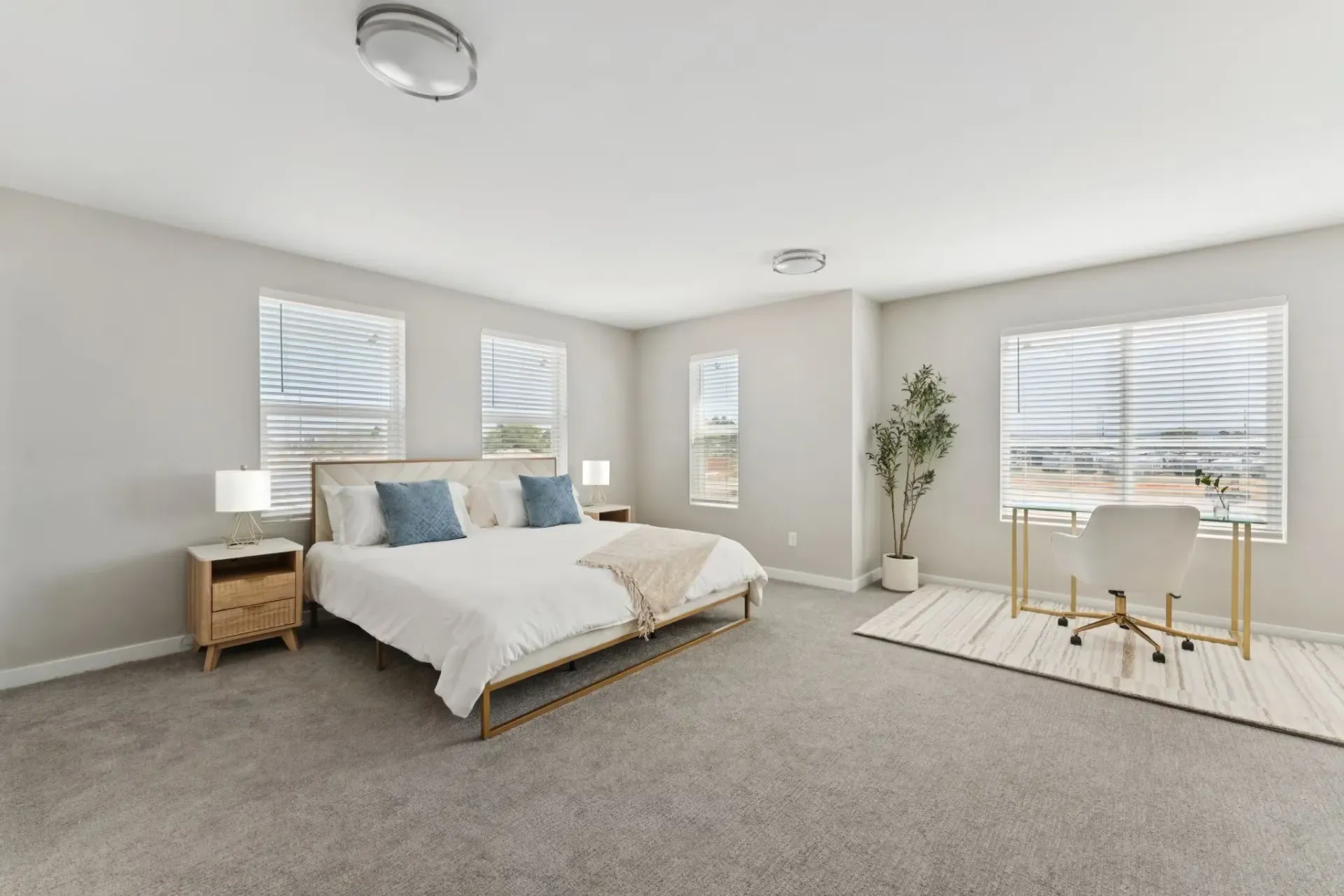 Bright modern bedroom with a queen bed, two nightstands, a desk by the window, and a potted plant.