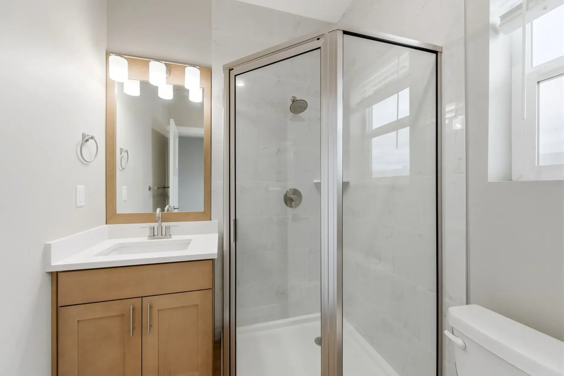 Bathroom with a glass-enclosed shower, white vanity, mirror, and toilet.