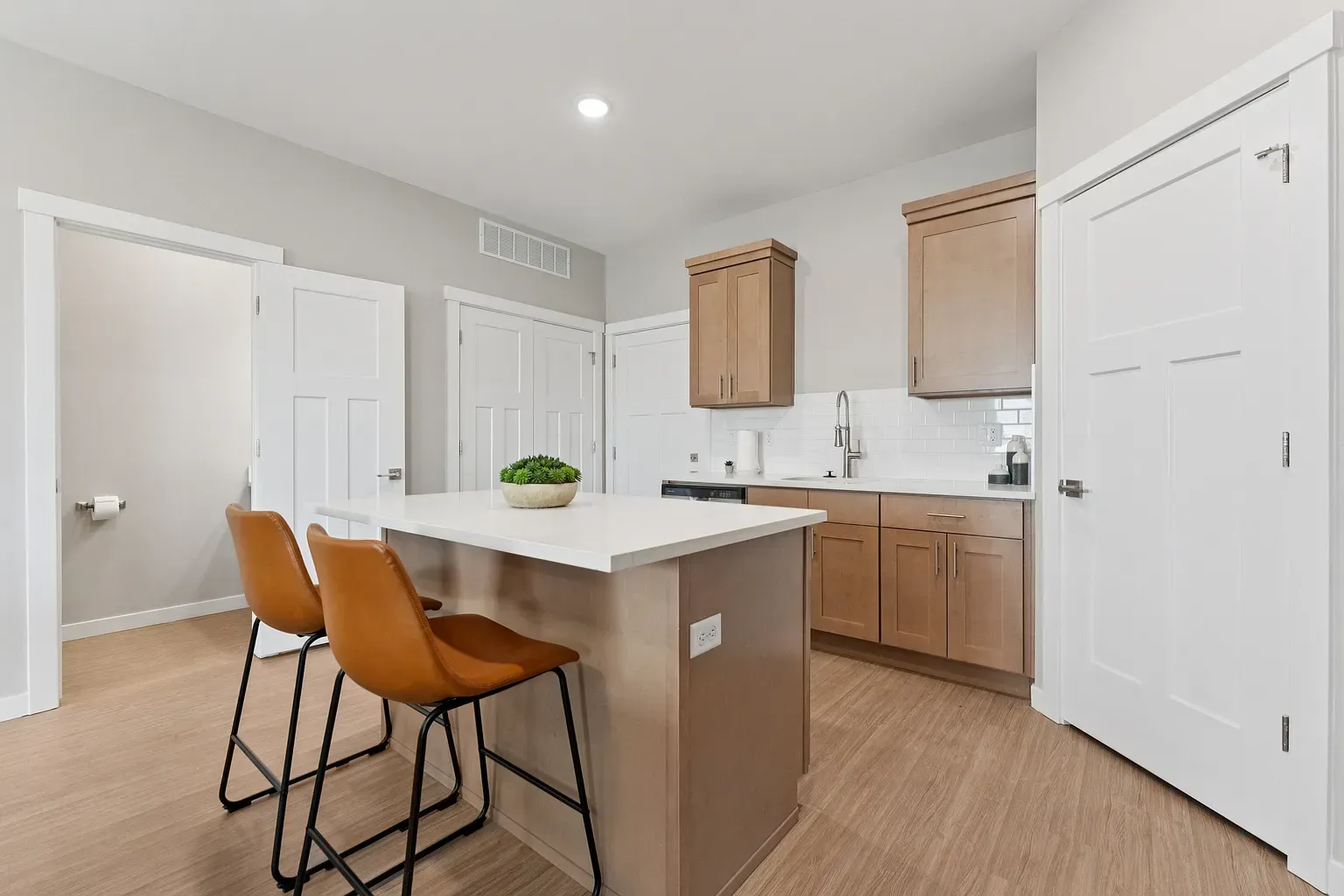 Modern apartment kitchen with island, white countertops, light wood cabinets, and bar stools.