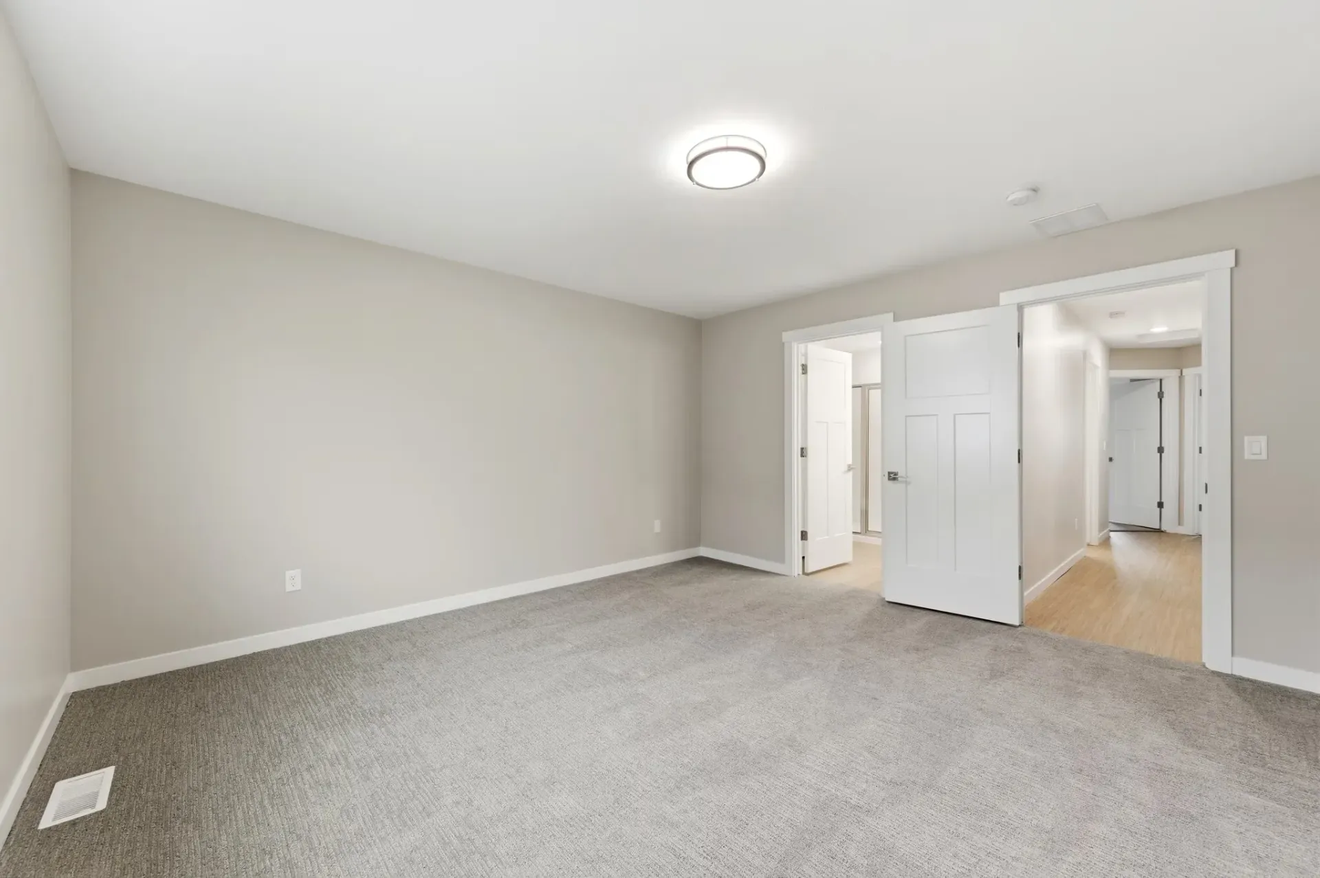 Empty neutral-toned bedroom with carpet and open doors to a hallway.