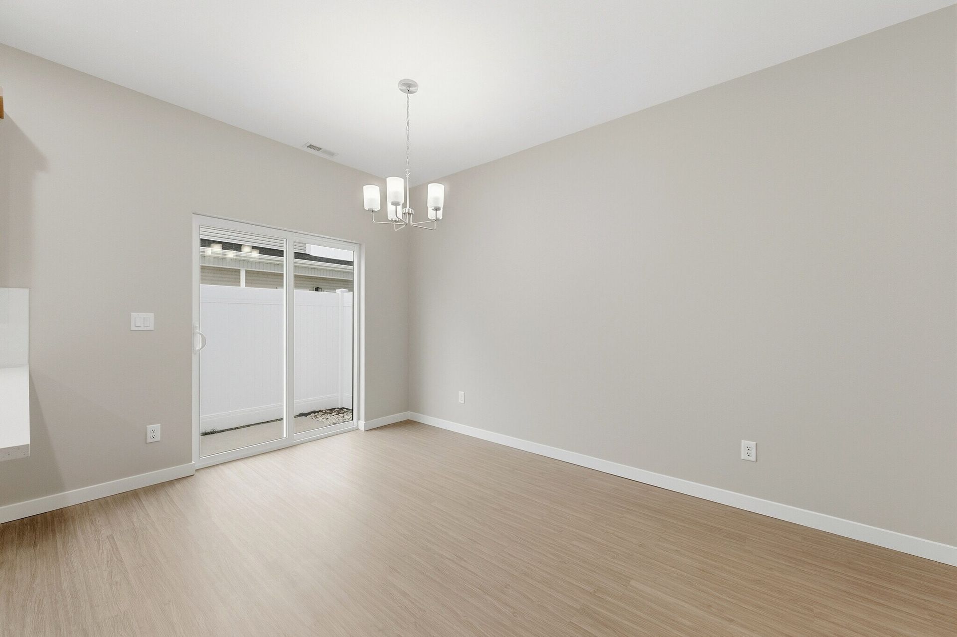 Empty living/dining area with sliding glass door to patio, neutral walls, and a contemporary chandelier.