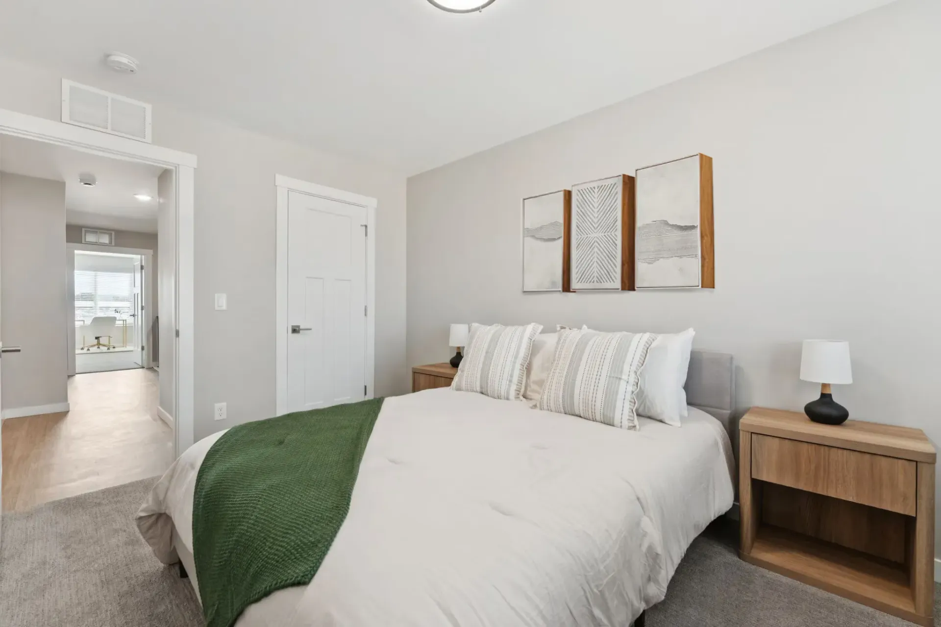 Bedroom inside an apartment with white bedding, a green throw, two wooden nightstands, and lamps.