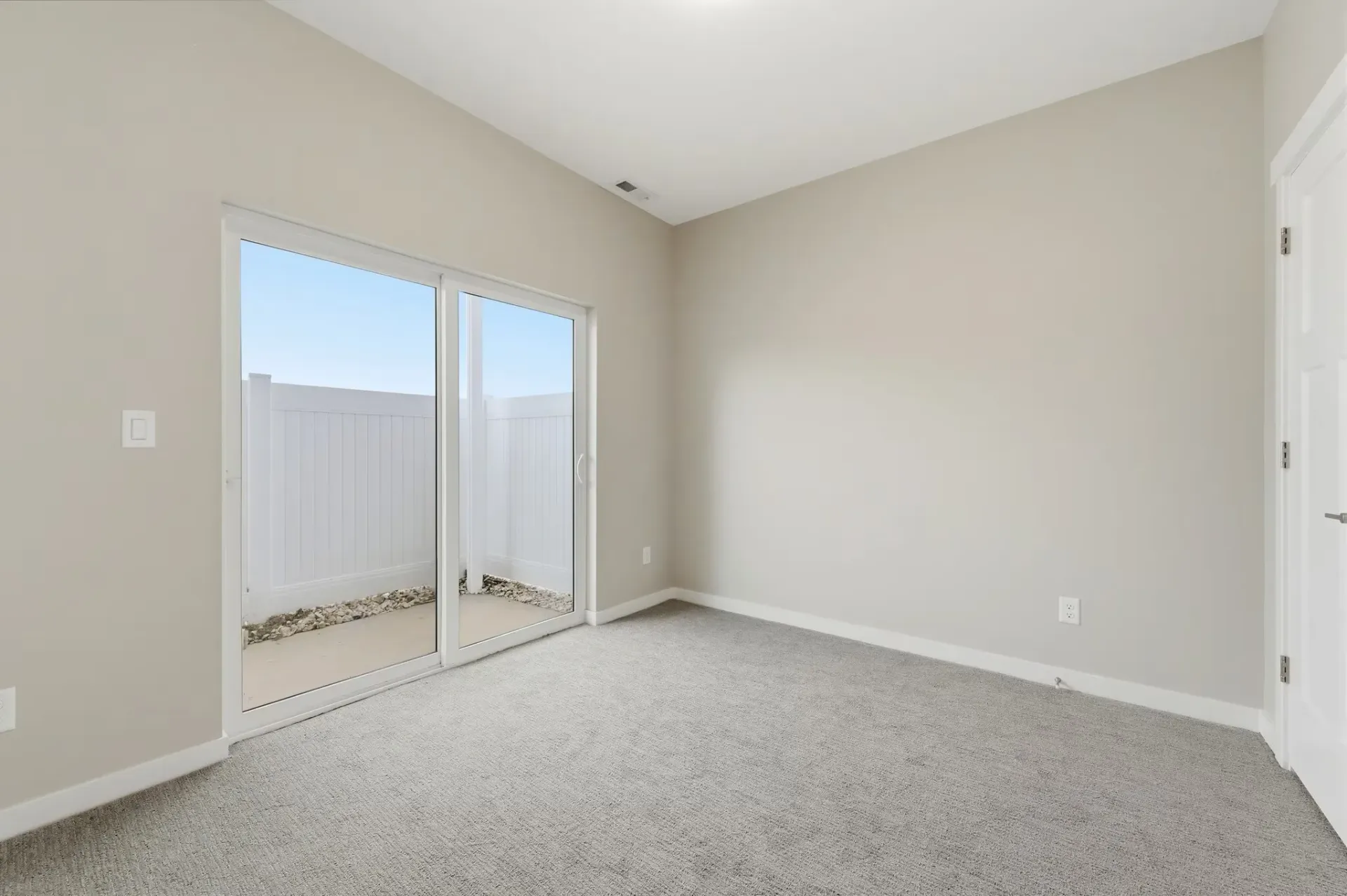 Bedroom with sliding glass door to small outdoor area, beige walls, carpet.