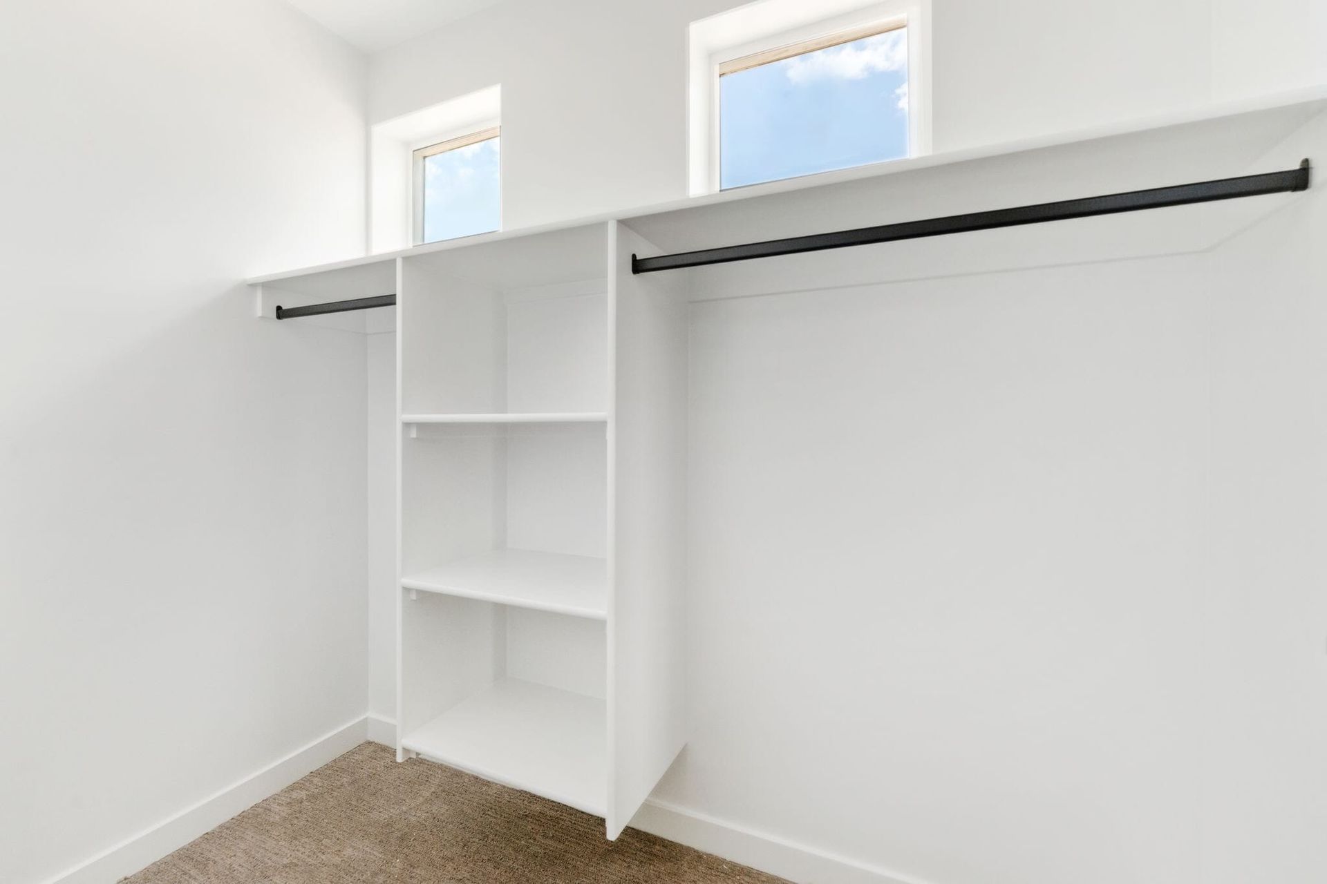 Bright white walk-in closet with built-in shelves and two hanging rods, plus small high windows.