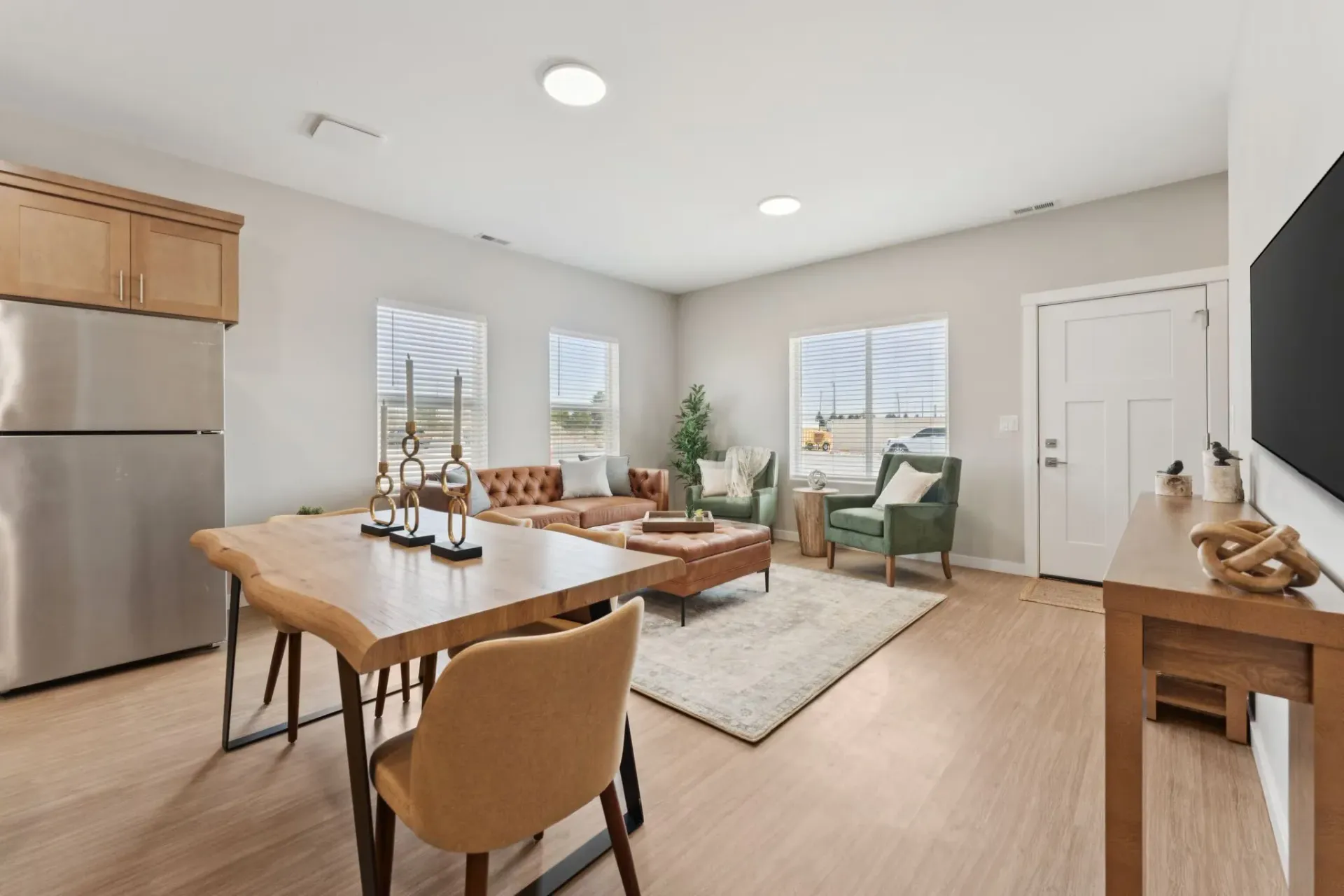 Open-concept living area with sofa, green chairs, dining table, and large windows.