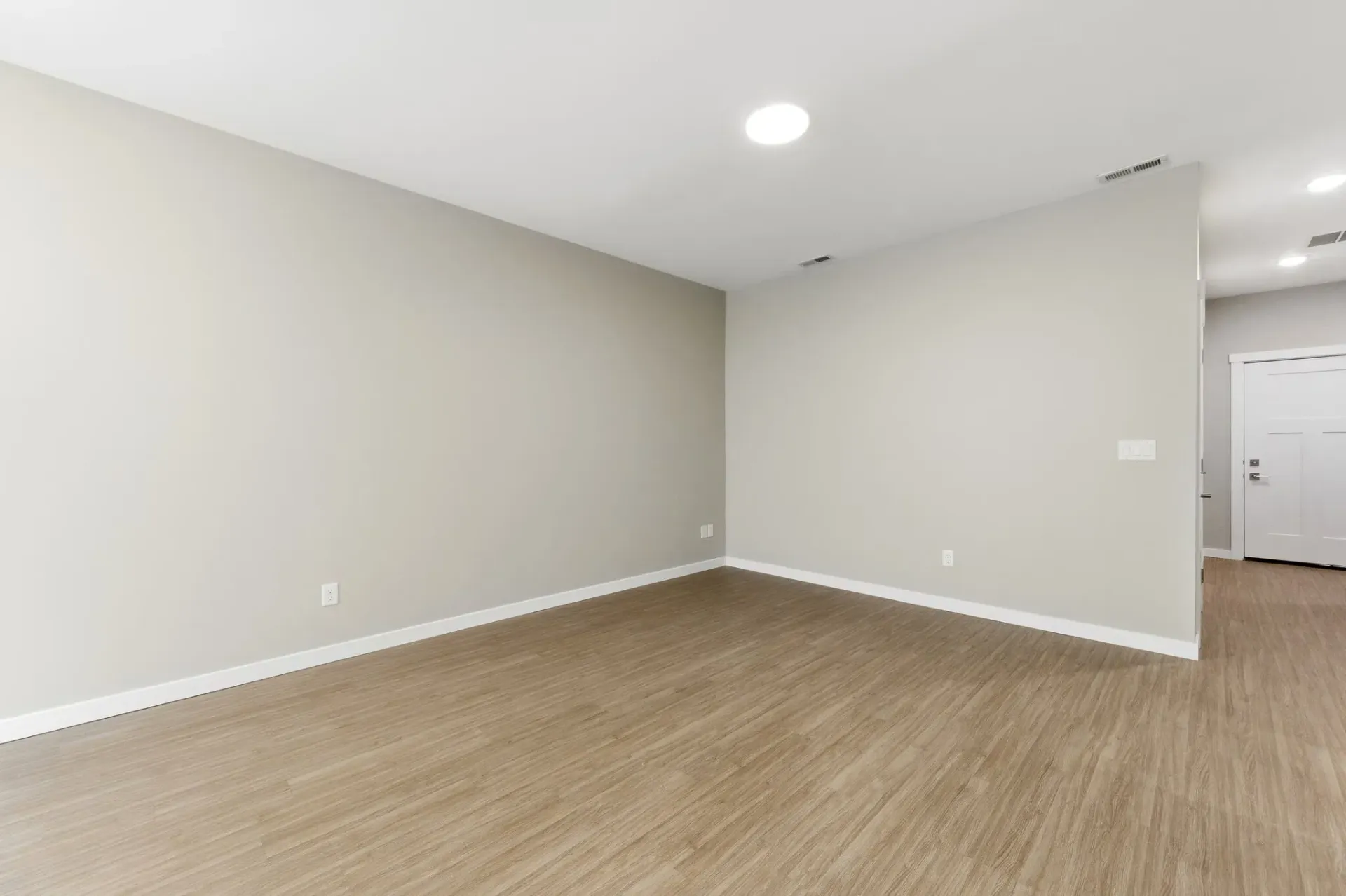 Empty living area in a modern apartment with beige walls and wood-look flooring.