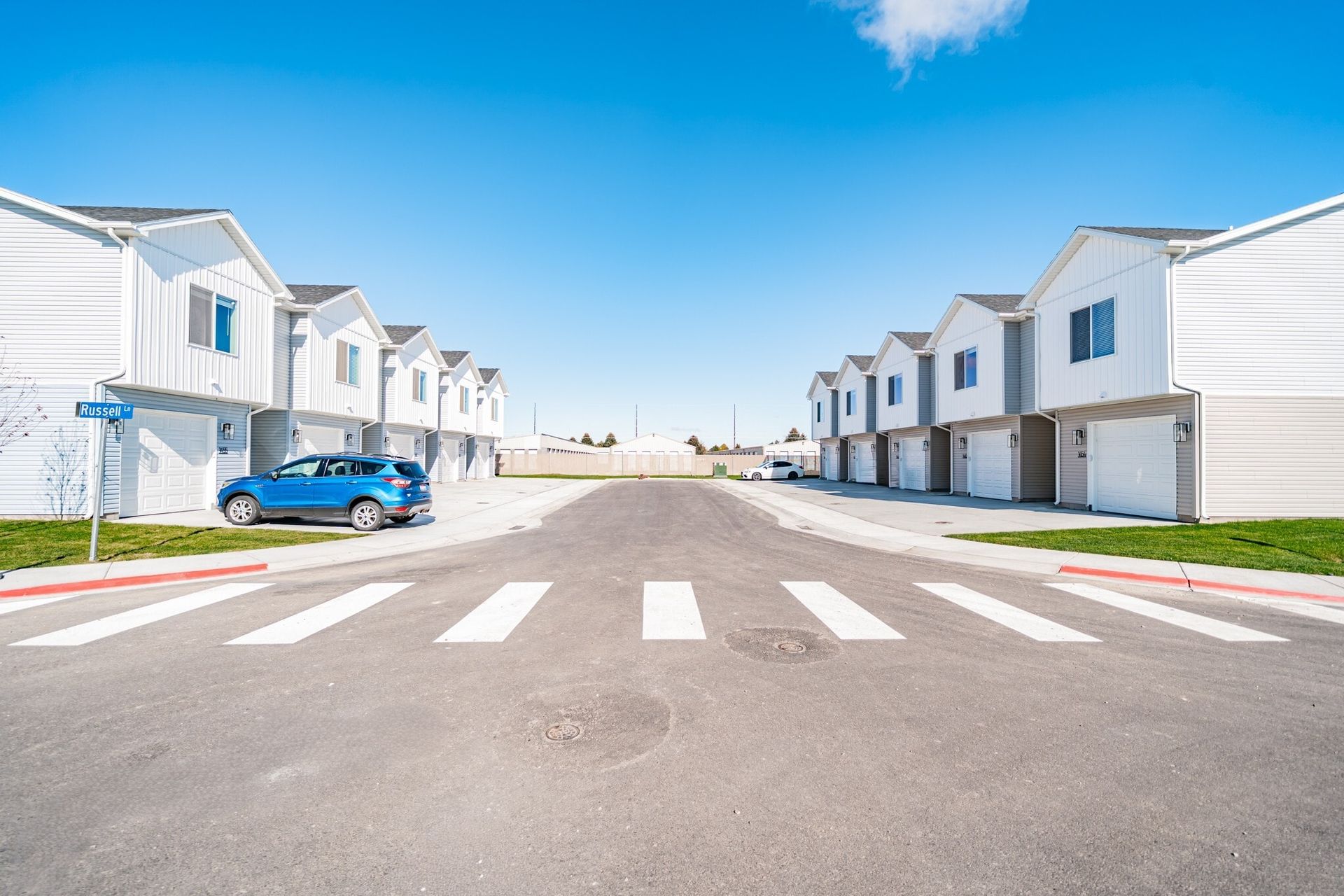 Row of white two-story townhomes with attached garages along a residential street under a blue sky.