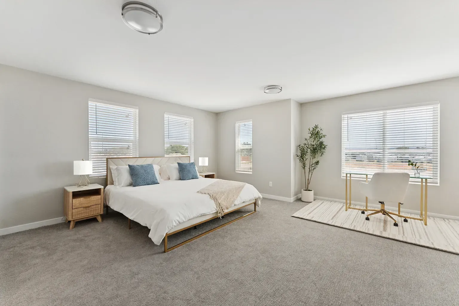 Bright modern bedroom in an apartment with a bed, two nightstands, and a desk by windows.