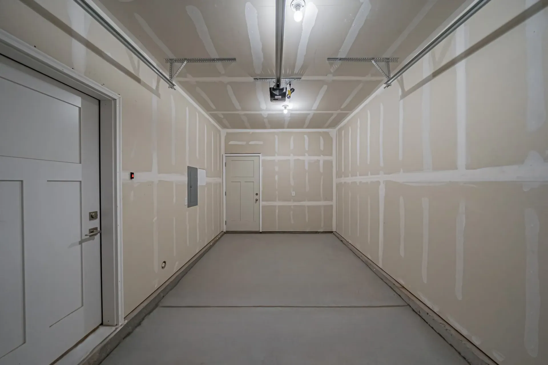 Unfinished garage interior with taped drywall seams and a single overhead light.