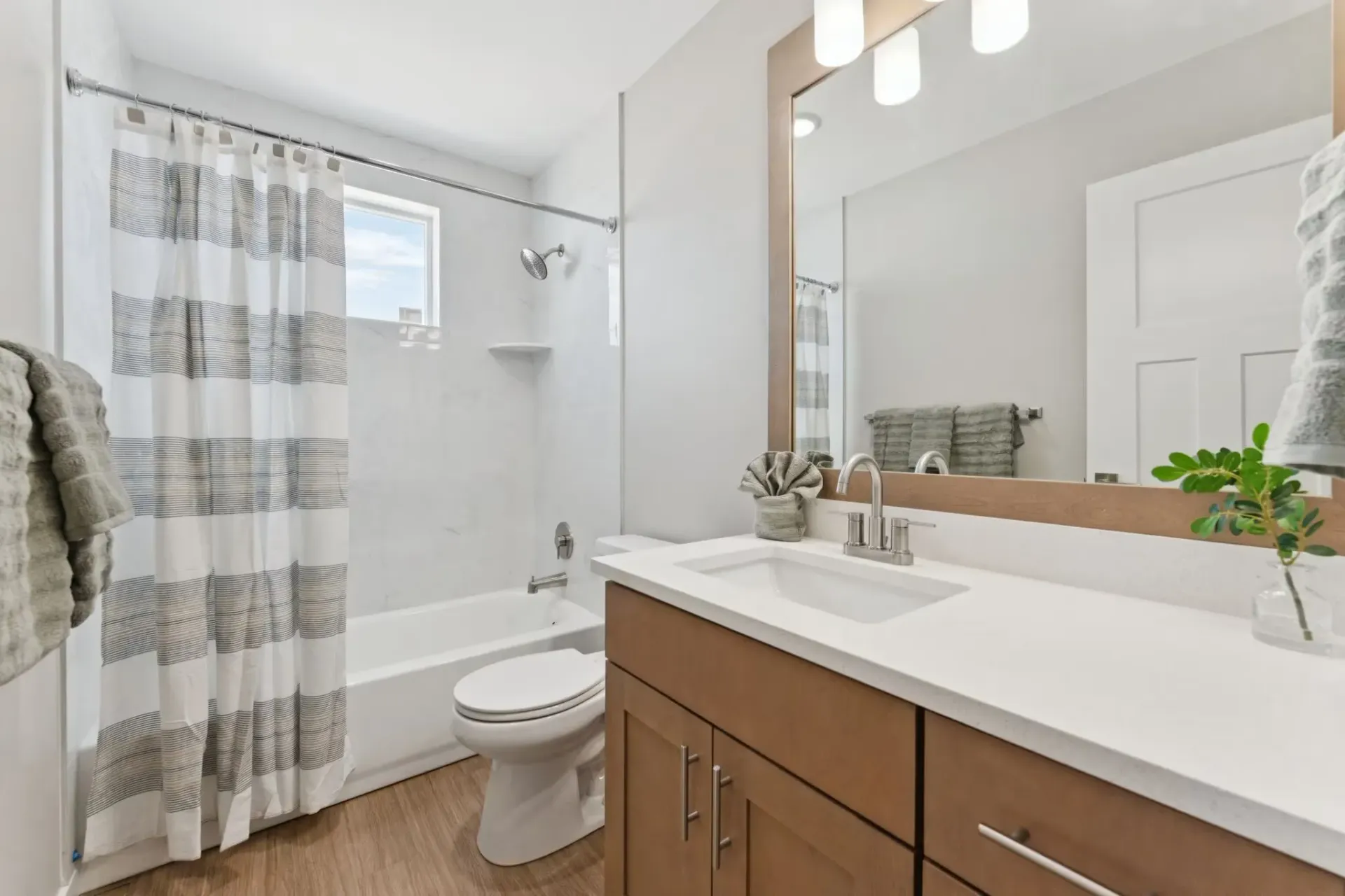 Modern apartment bathroom with vanity, sink, mirror, toilet, and a striped shower curtain.