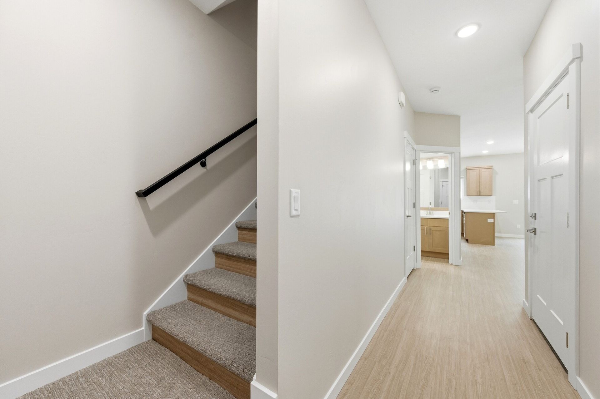 Interior hallway with staircase on the left and doorway to a kitchen area ahead.