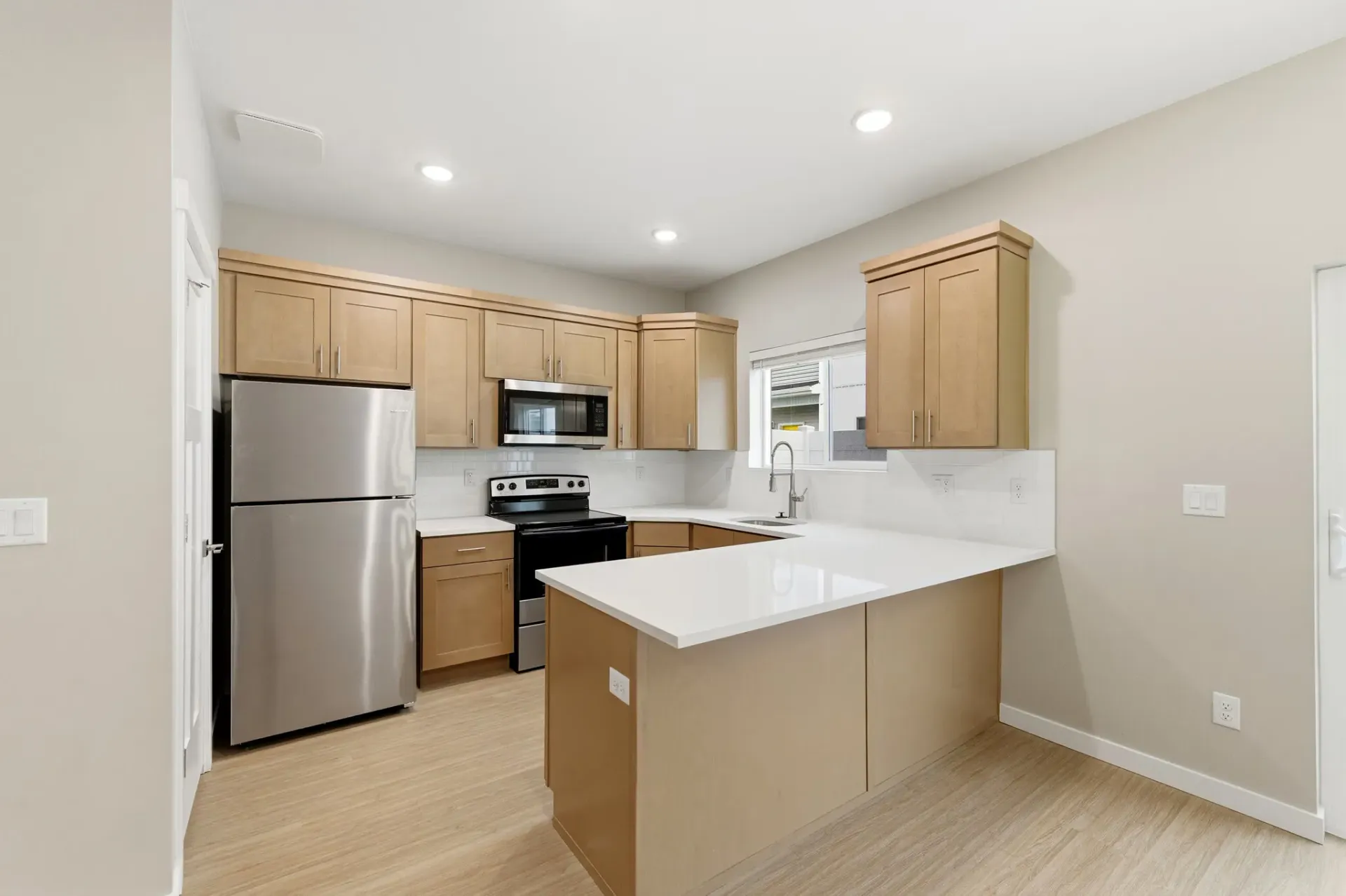 Modern apartment kitchen with stainless steel appliances, light wood cabinets, and an island.