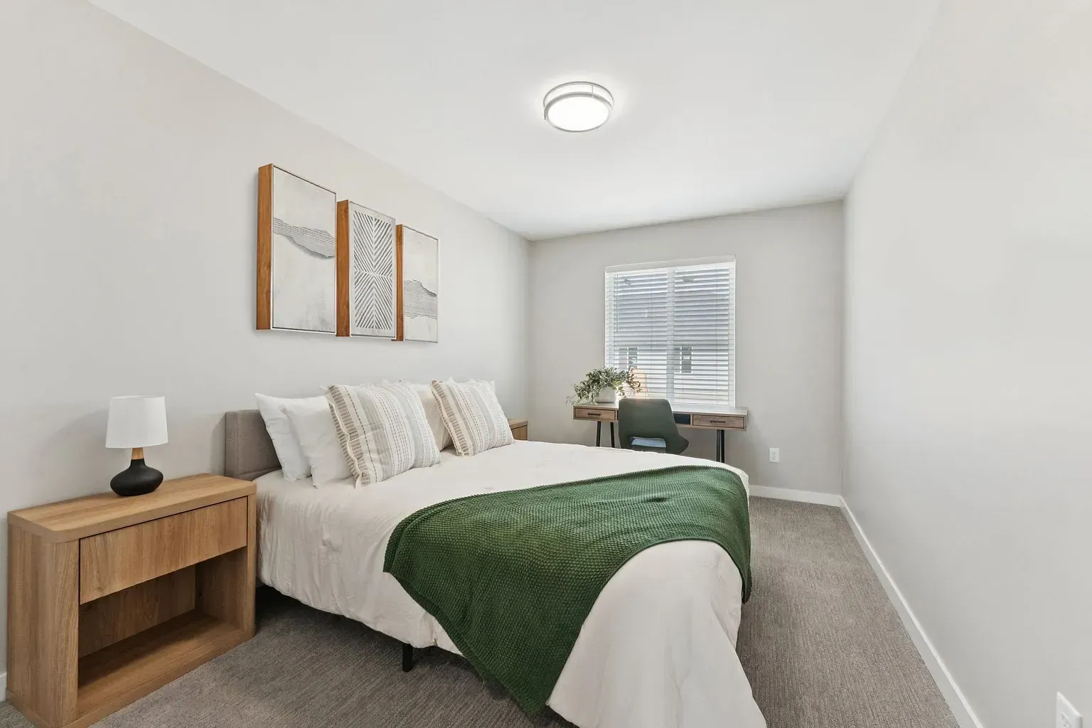 Bedroom in a modern apartment with a bed, nightstand, and a desk near a window.