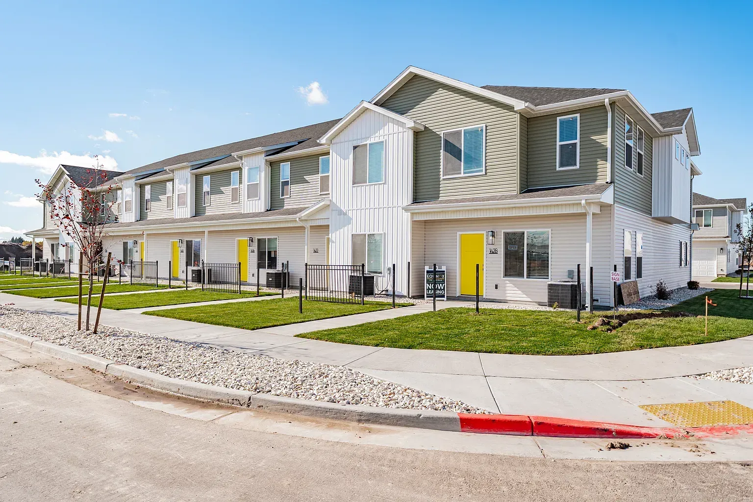 Exterior view of a row of townhomes with yellow doors and green lawns.