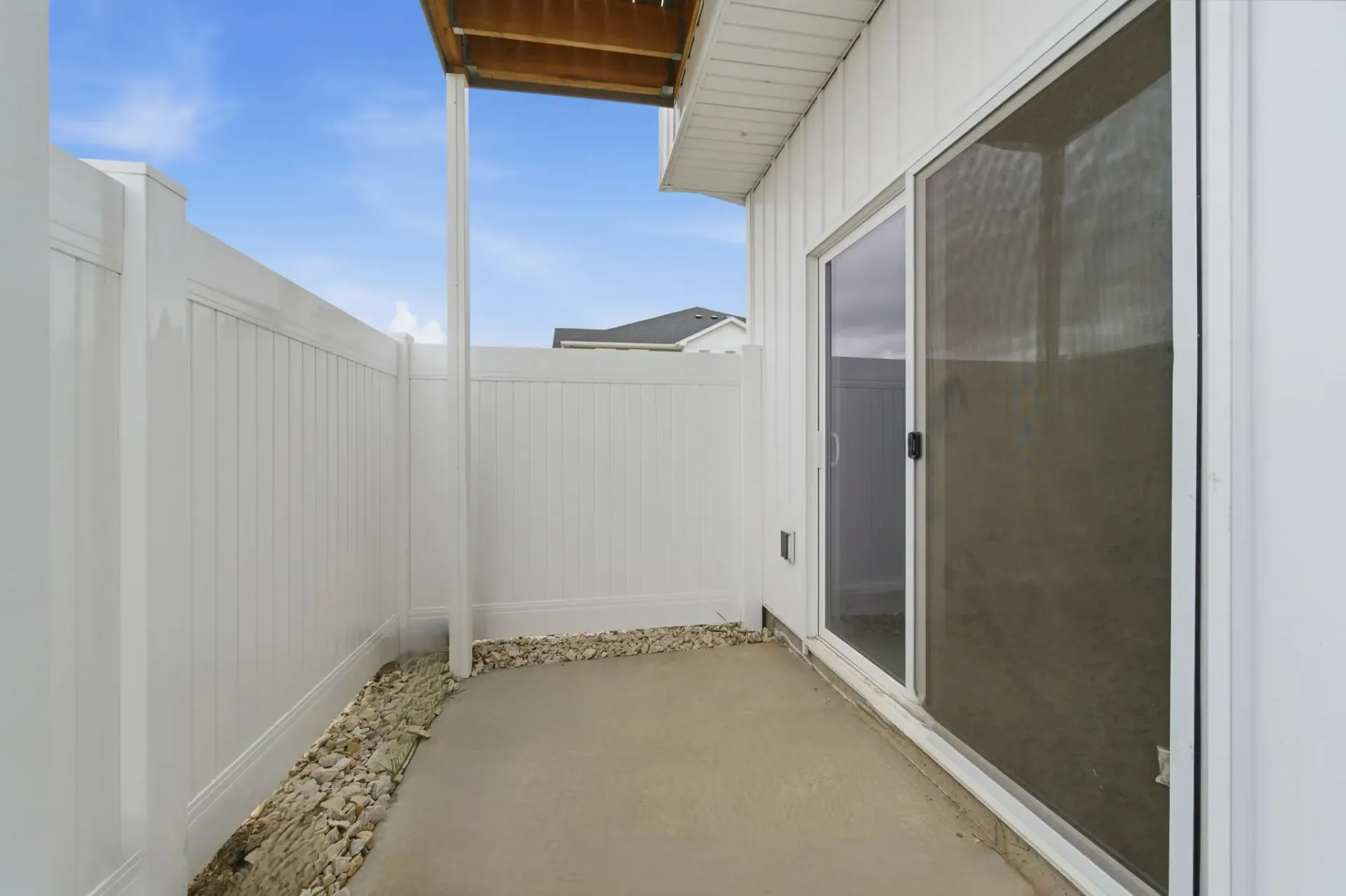 Ground-level patio with white vinyl privacy fence, sliding glass door, and gravel border.