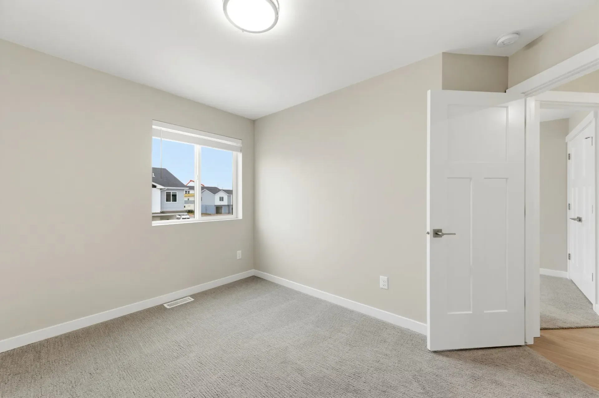 Vacant bedroom with beige walls, carpet, a window, and a white door.