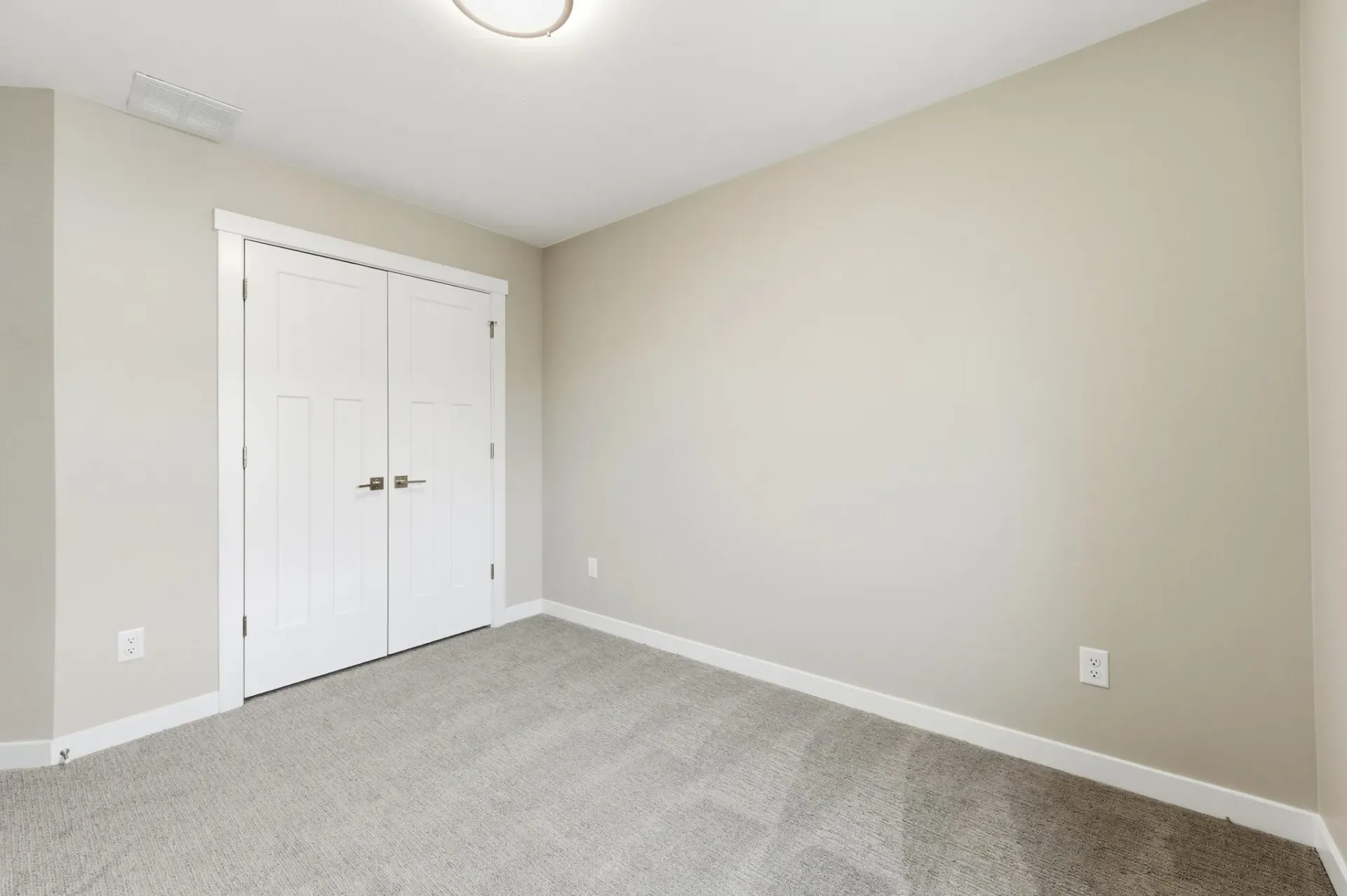 Empty beige bedroom with white double-door closet and neutral carpet.