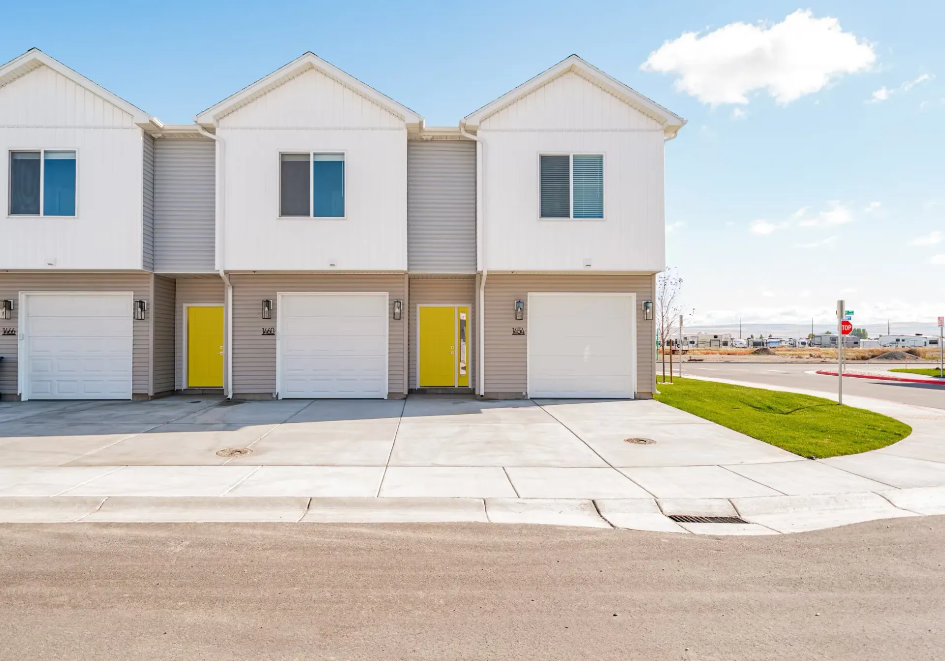 Exterior view of a row of townhome-style buildings with attached garages and yellow entry doors.
