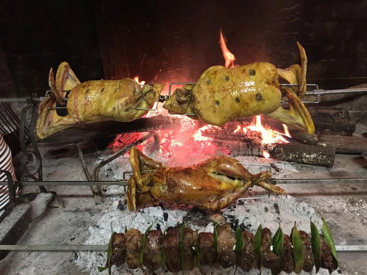 Pesce intero e carne allo spiedo arrostiti su una griglia a fuoco vivo.