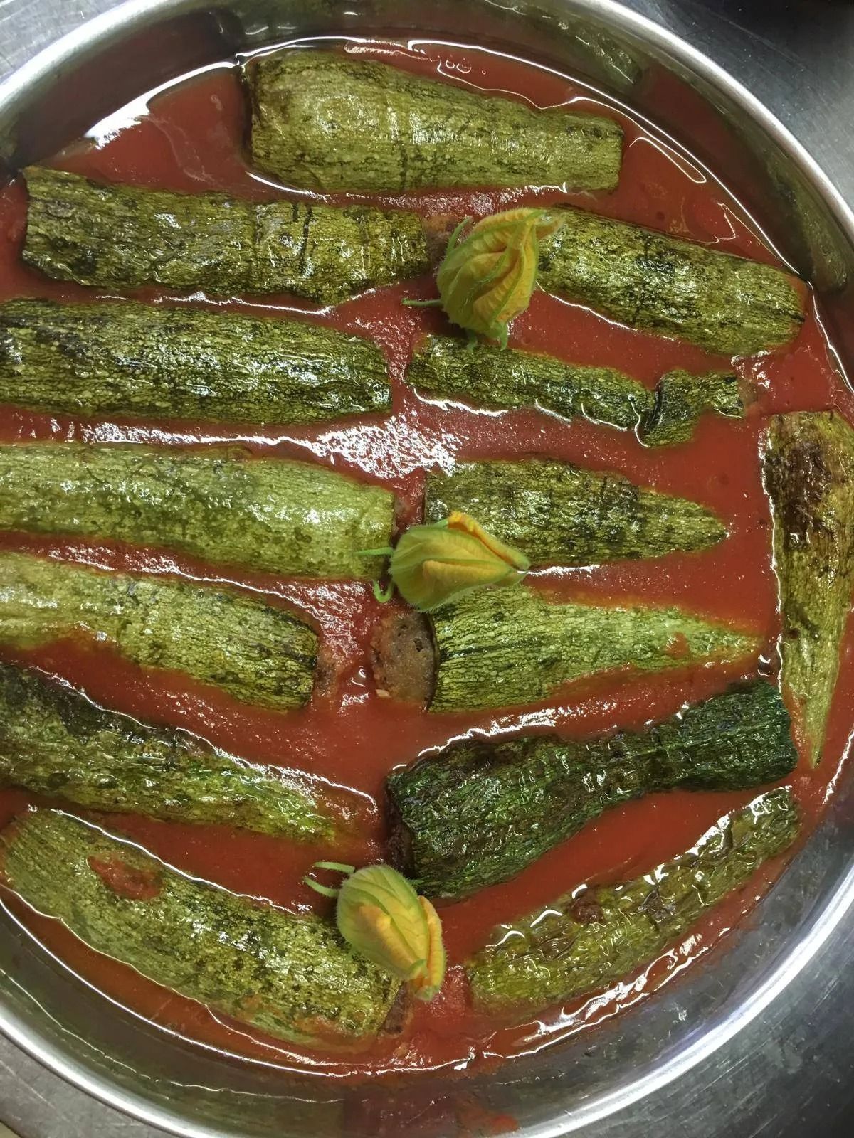 Vassoio rotondo in acciaio con verdure verdi ripiene in salsa rossa, guarnito con peperoncini verdi.
