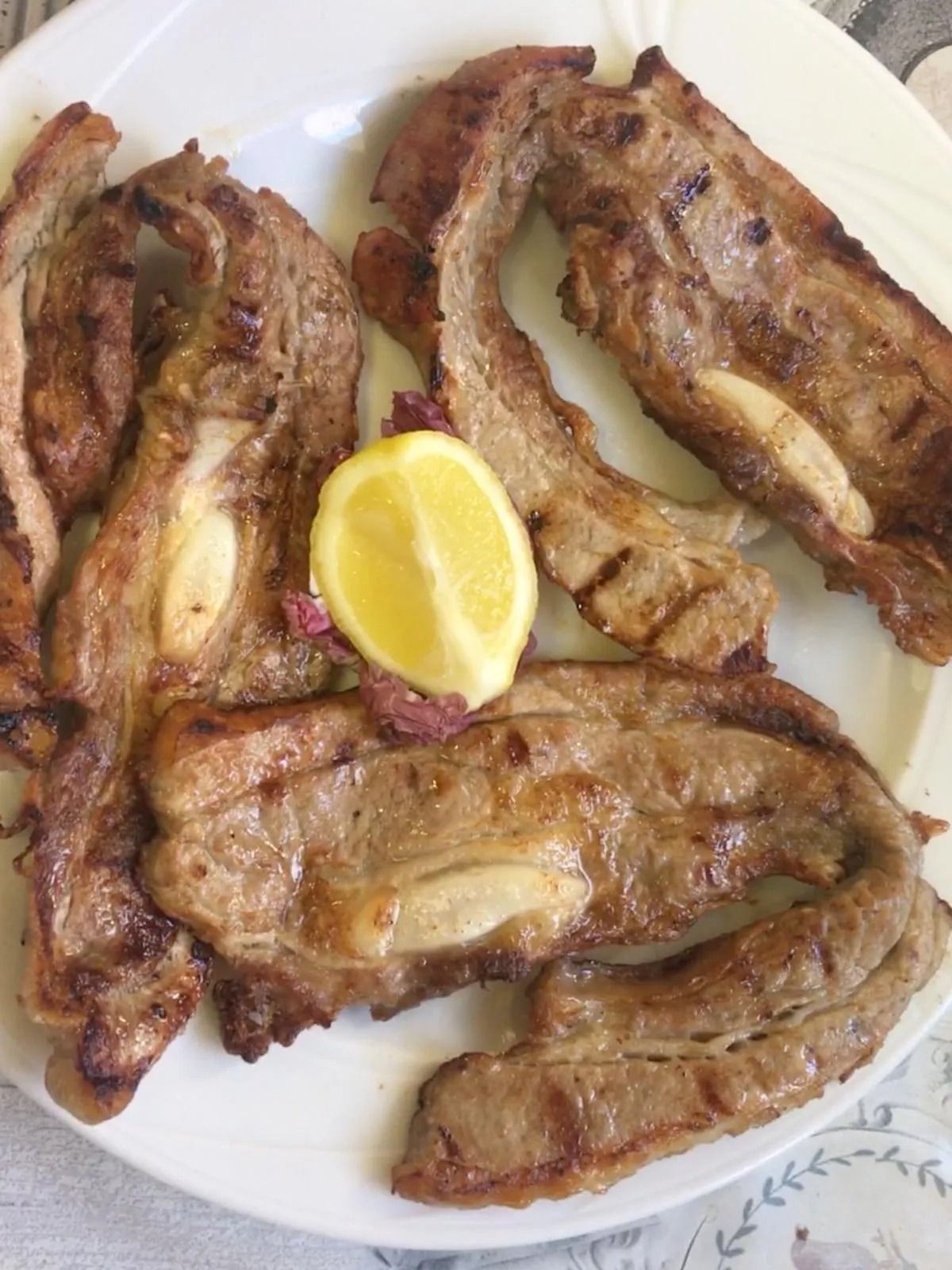 Piatto di pezzi di carne grigliata con uno spicchio di limone su un piatto bianco.