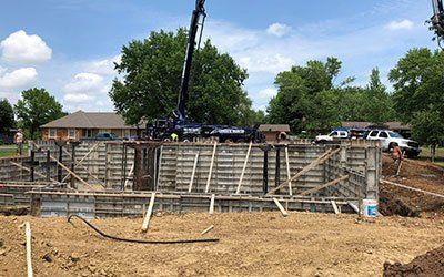 A crane is pouring concrete into a foundation of a house.