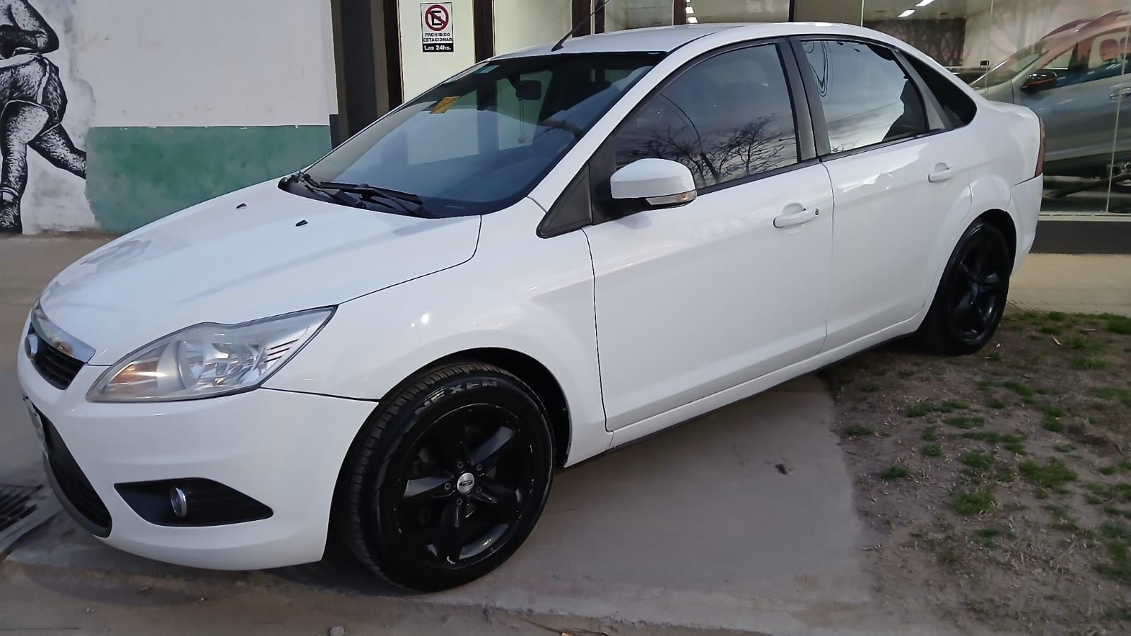 Sedán Ford Focus blanco con llantas negras estacionado afuera.