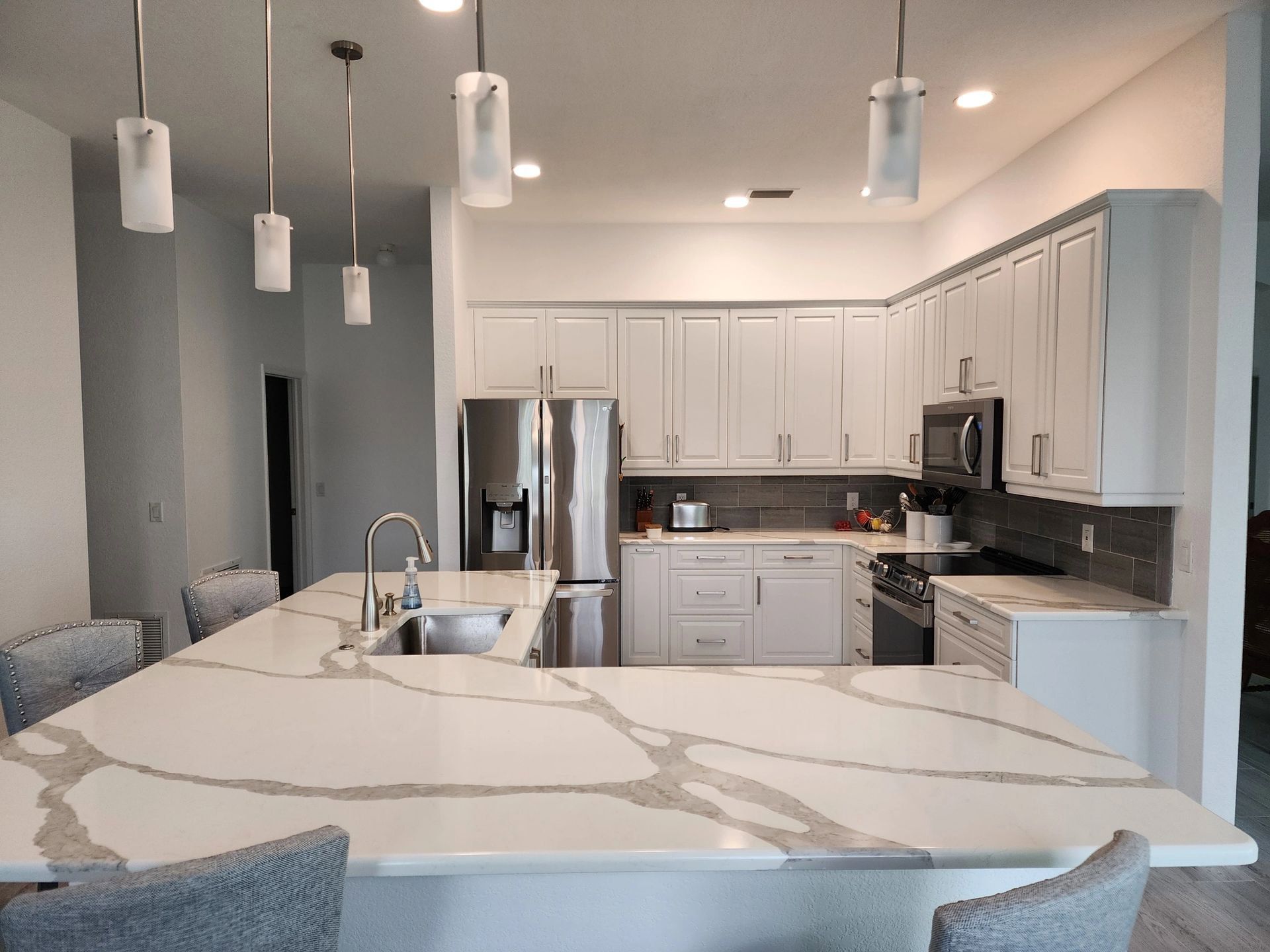 A kitchen with white cabinets, granite counter tops, stainless steel appliances and a large island