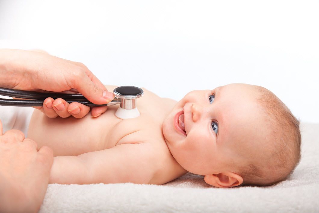 A pediatrician listening to the heartbeat of a smiling baby