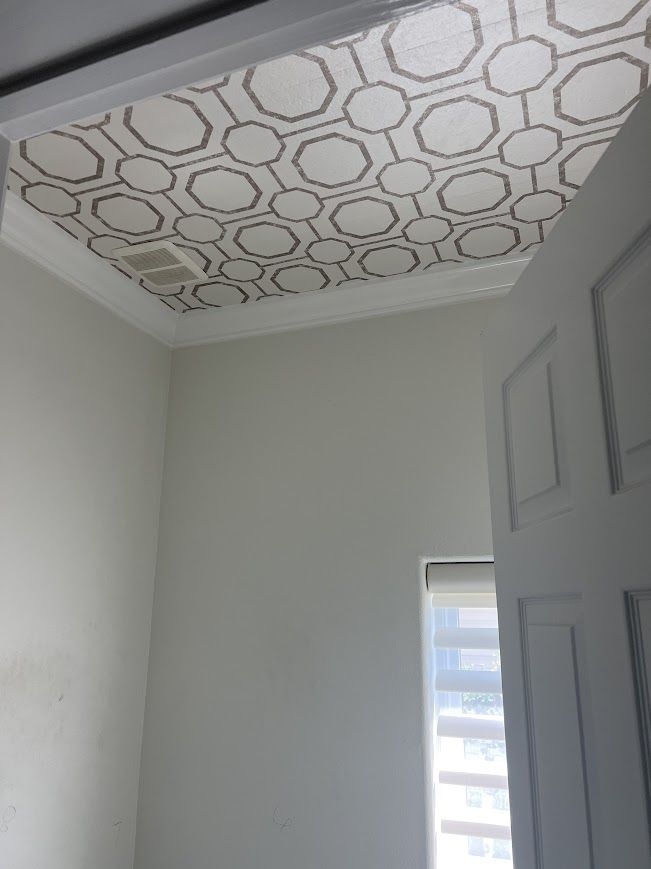 Room interior with patterned ceiling, white walls, open door, window with blinds.