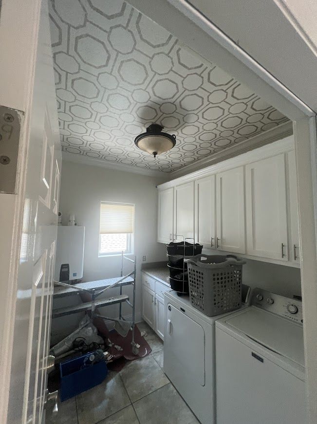 Laundry room with white cabinets, appliances, and a patterned ceiling.