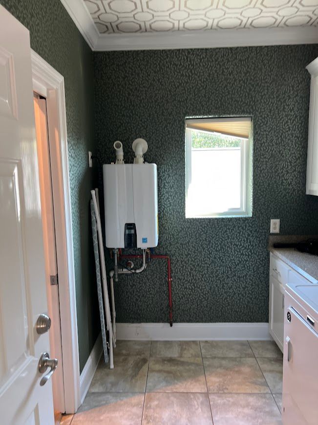 Small utility room with a tankless water heater, window, cabinets, and a door.