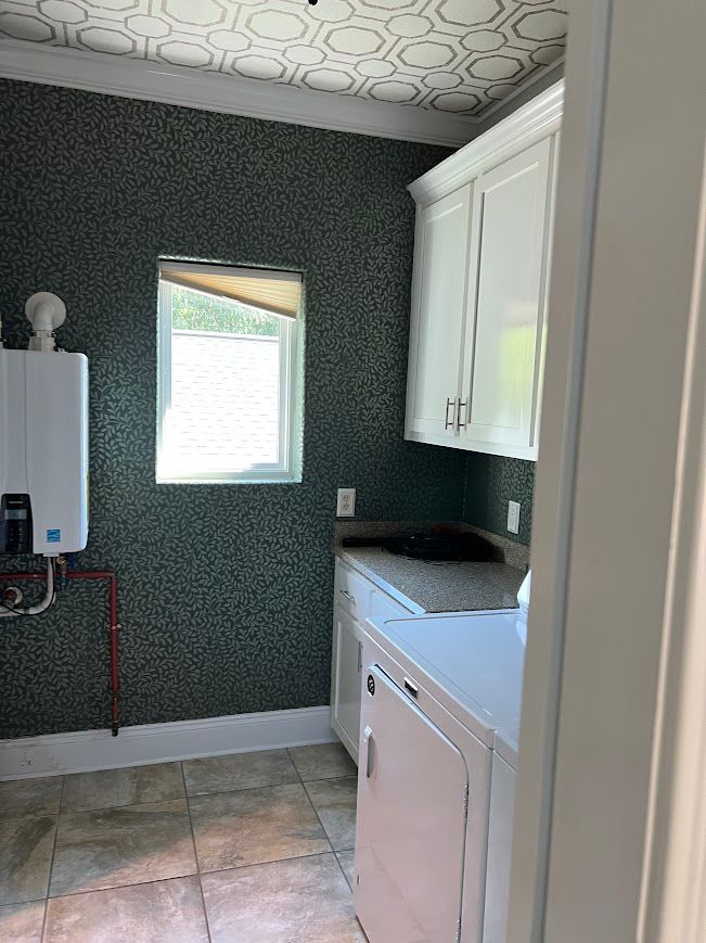 Laundry room with patterned green wallpaper, white cabinets, and a window.