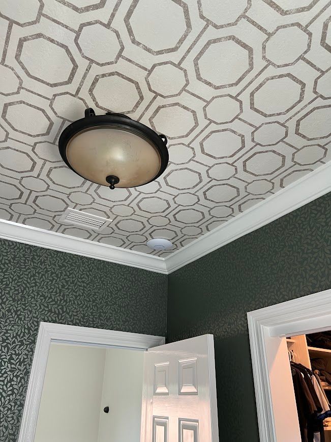 Room interior with geometric ceiling design and dark green walls. A light fixture is mounted on the ceiling.
