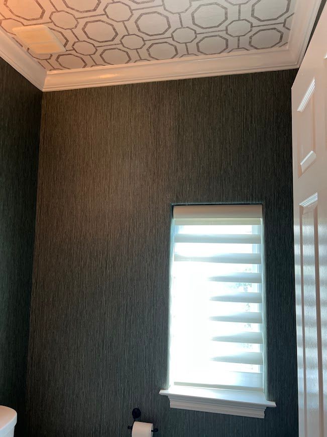 Dark grey textured wallpaper in a room with a white door and window with closed blinds. Decorative ceiling pattern.