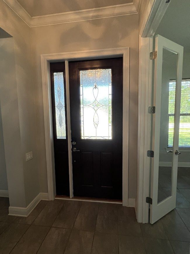Entryway with dark brown front door, sidelight, and white-framed glass doors leading to a room.