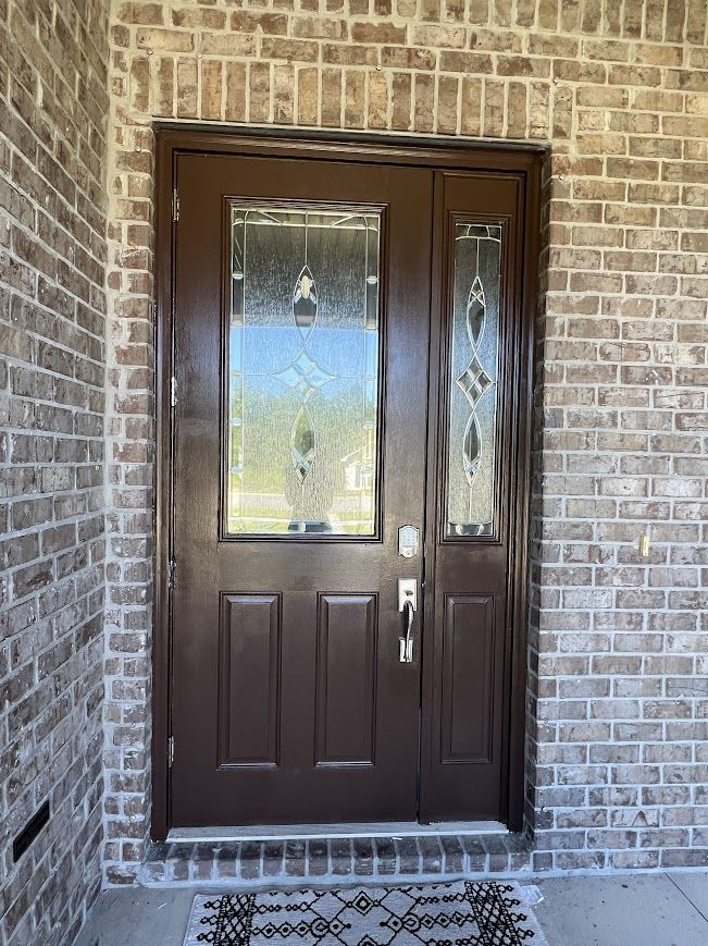 Brown front door with glass panels set in a brick wall. A small rug lies on the porch.