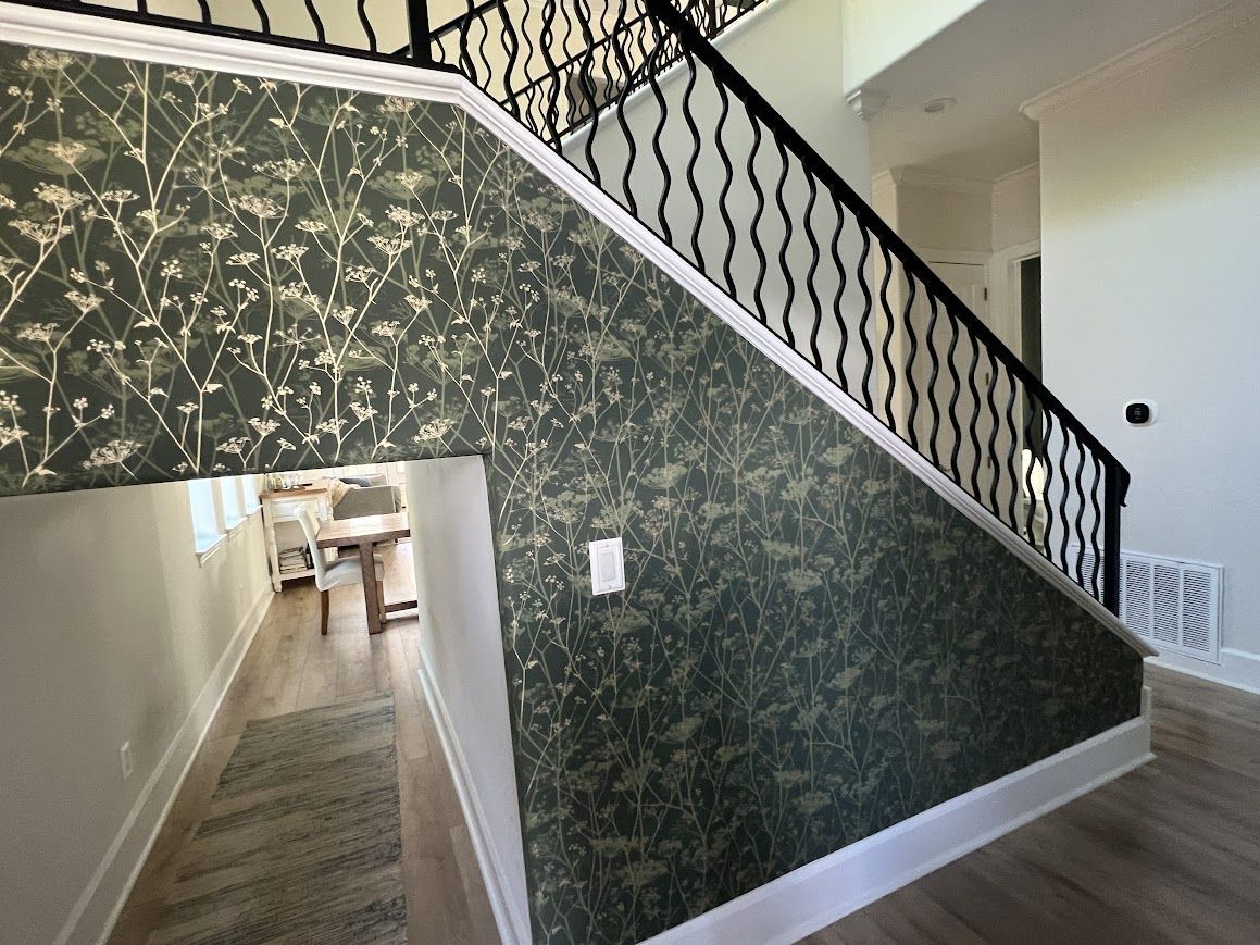 Stairwell with green floral wallpaper, black railing, white trim, and light wood flooring.