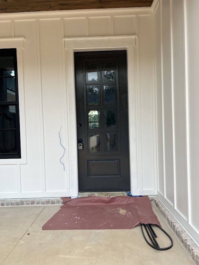 Black front door with glass panels on a white paneled building exterior, a red mat in front.