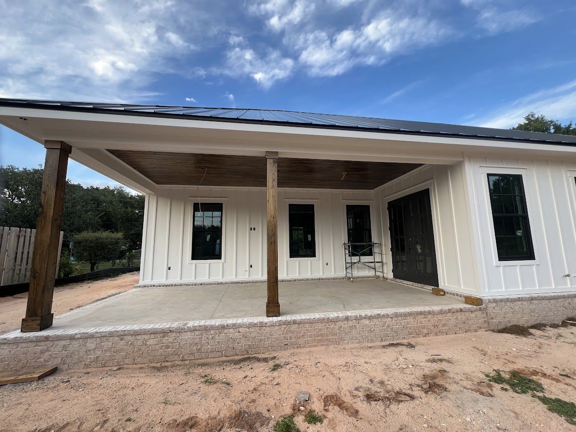 White house with porch and dark-framed windows, supported by wooden pillars; on a sunny day.