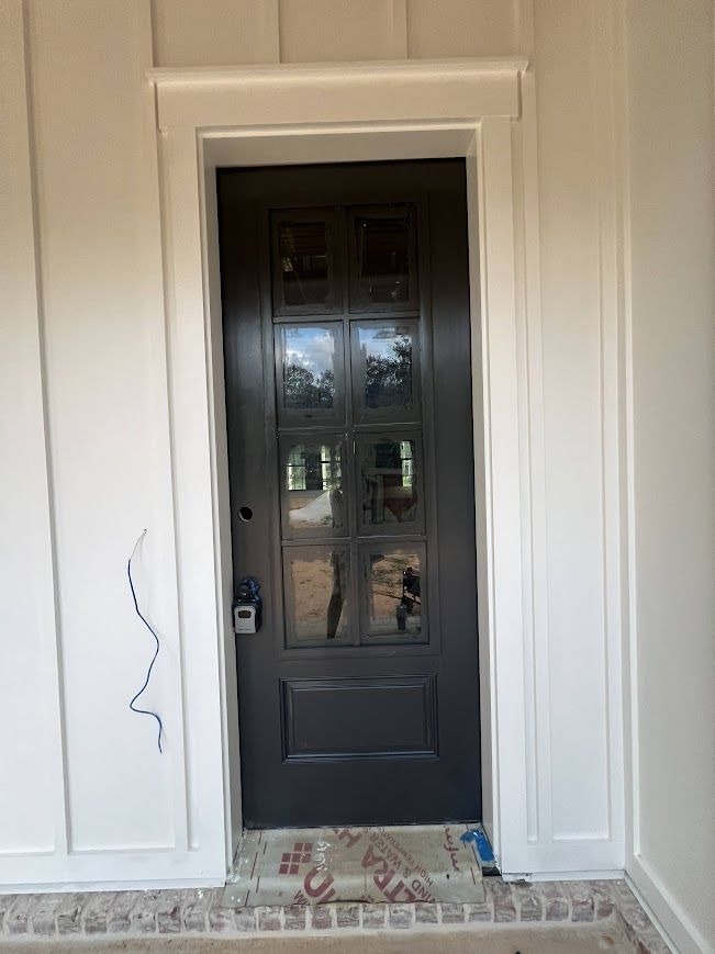 Dark gray front door with glass panels framed by white trim on a white exterior wall.