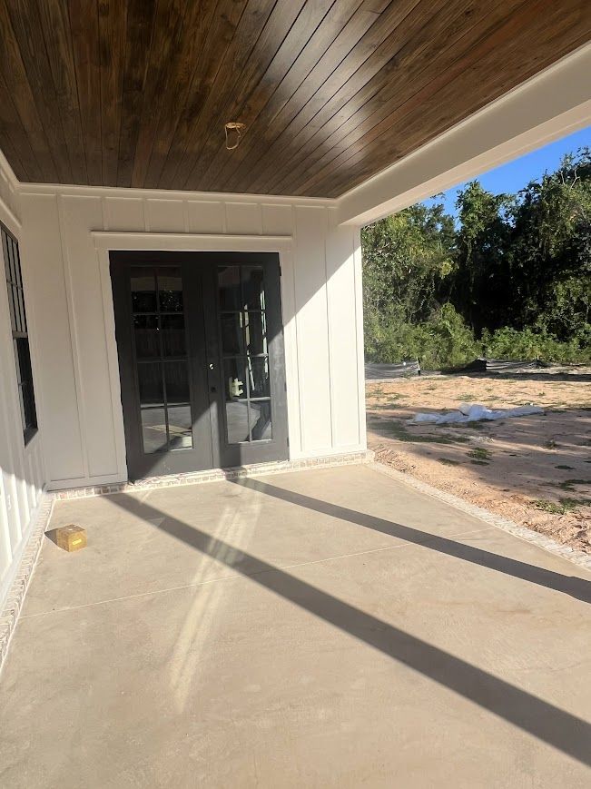 Covered porch with dark doors, white siding, and a stained wood ceiling.